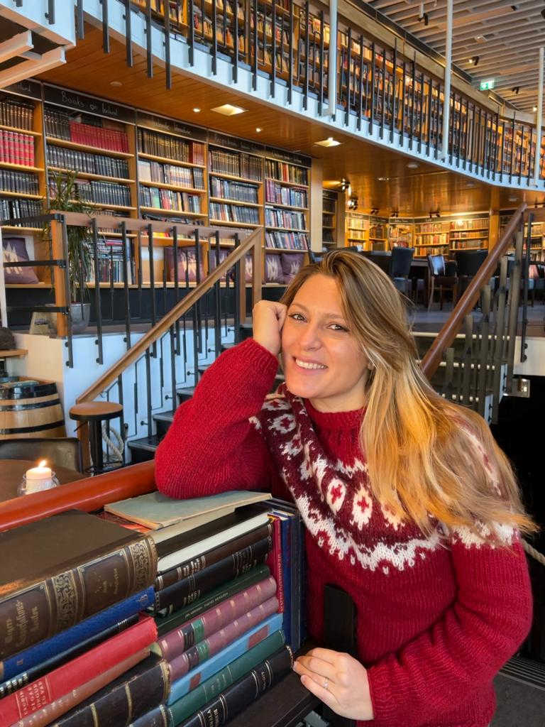 Donna sorridente con capelli lunghi biondi seduta in biblioteca